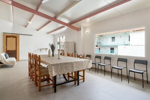 A dining area with a table and chairs, a wooden bench, a refrigerator, and a window with a view of buildings.