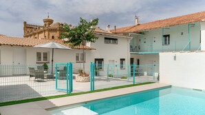 A residential property with a swimming pool, a fenced patio area, and a traditional building with a tiled roof.