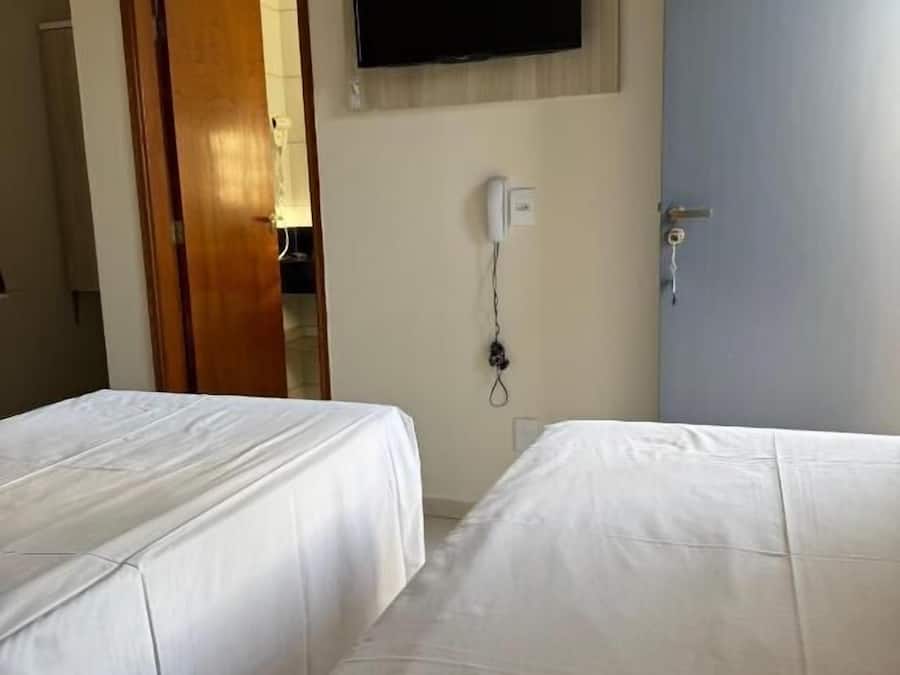 Habitación de hotel con dos camas, un televisor montado en la pared, una puerta y un teléfono en la pared.