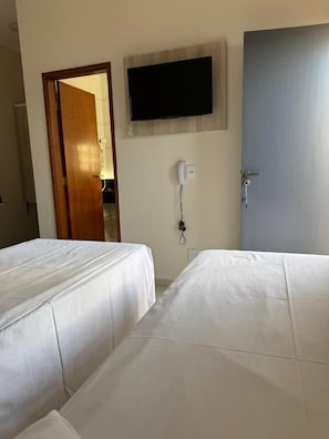 Habitación de hotel con dos camas, un televisor montado en la pared, una puerta y un teléfono en la pared.