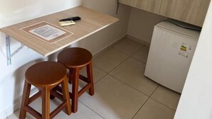 Una pequeña kitchenette con una mesa de madera, dos taburetes y un refrigerador.