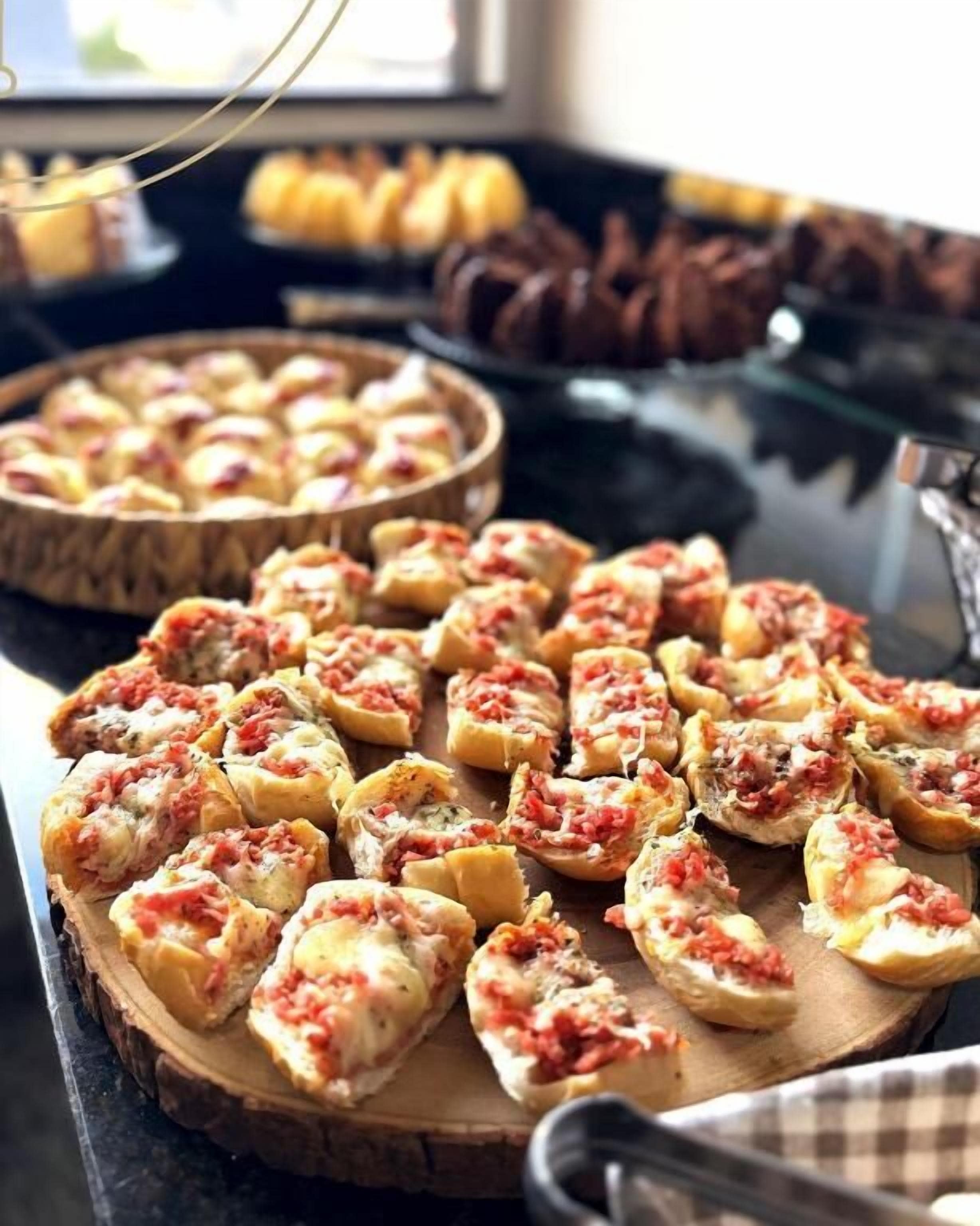 Un bufé con distintos alimentos, incluyendo una amplia tabla de madera con pan cubierto de salsa roja.