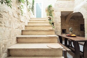 Un escalier en pierre mène à une pièce où se trouve une table en bois et une assiette de fruits.