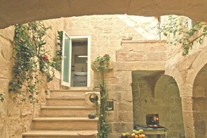 Un escalier en pierre mène à une pièce dotée d’une fenêtre, d’une cheminée et d’un panier de fruits.