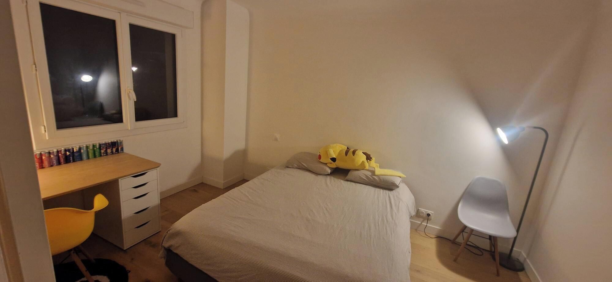A bedroom with a bed, a desk with a chair, a window, and a lamp.