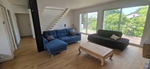 Ein geräumiges Wohnzimmer mit Holzboden, einem blauen Sofa, einem dunklen Sofa und einem Couchtisch aus Holz.