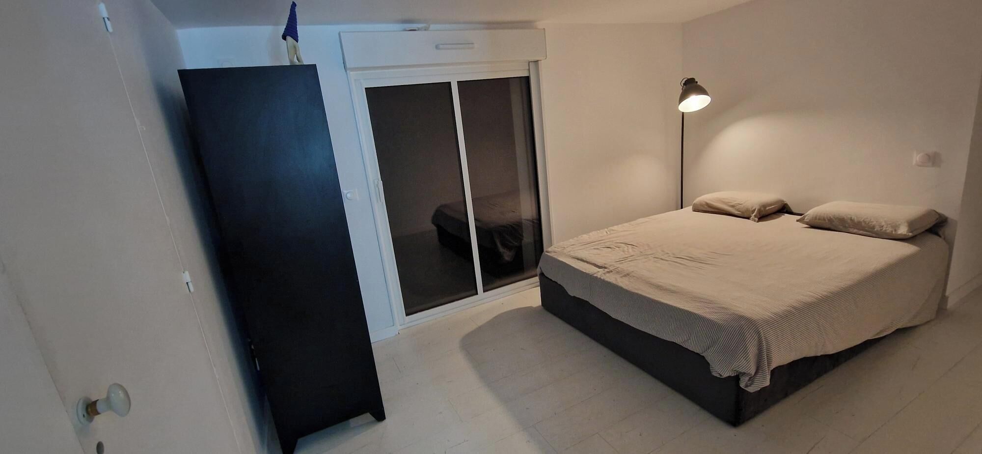 A bedroom with a bed, a nightstand, a lamp, a sliding door, and a wardrobe.