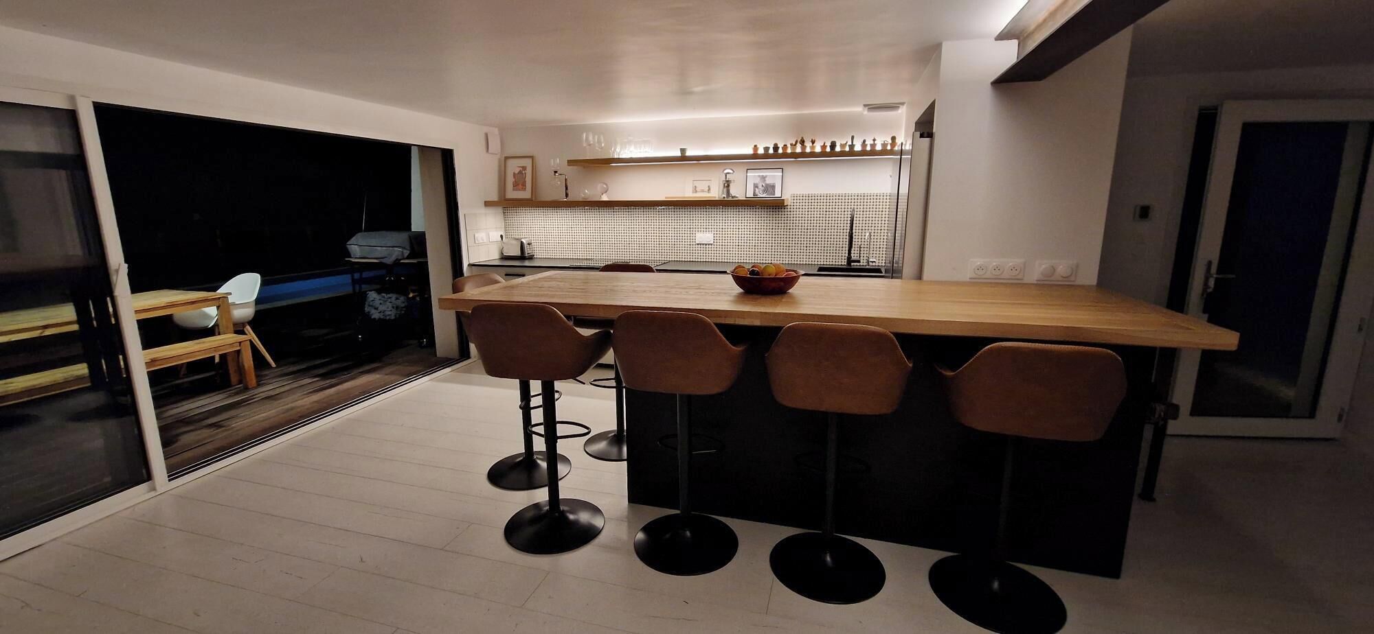 Una cocina moderna con una isla de madera, taburetes de bar y un comedor con mesa y sillas.