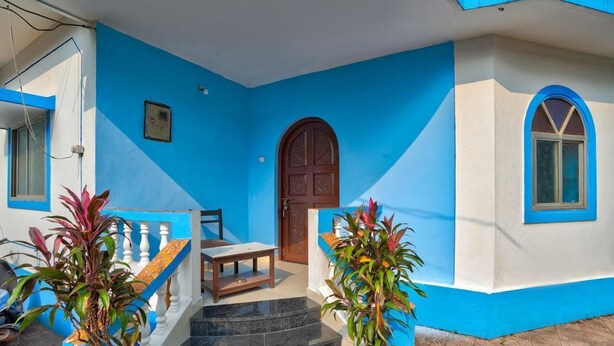 Un bâtiment à la façade bleue et blanche, avec une porte en bois et un escalier menant à l’entrée.