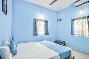 A bedroom with a bed, two windows with curtains, an air conditioner, and a small table. - Close to Beach 2BHK Villa (Calangute)