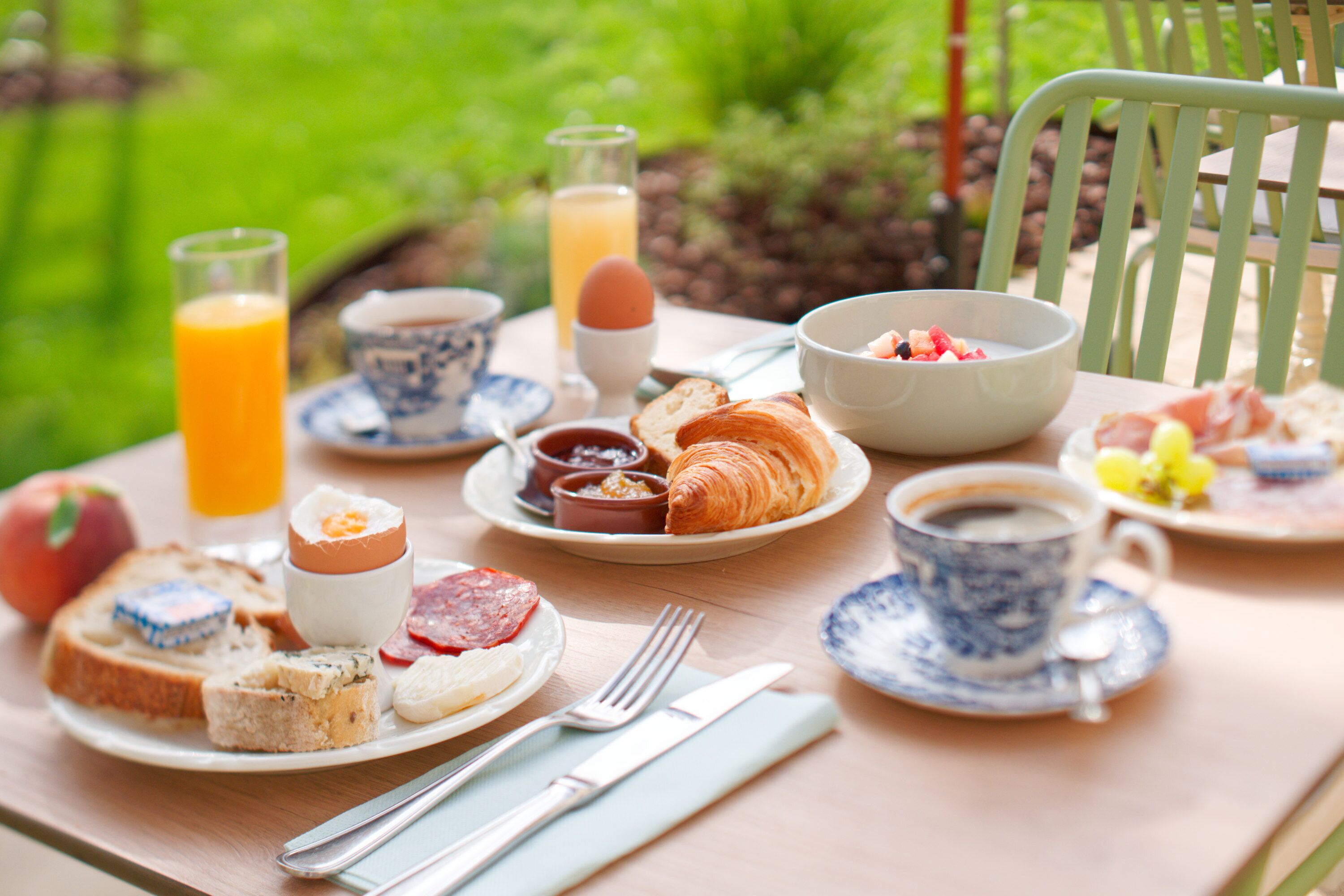 A breakfast table with plates of food, a glass of orange juice, a cup of coffee, and a bowl of fruit.