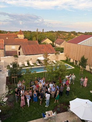Un grupo de personas reunidas en un patio trasero con una piscina, rodeado de edificios de piedra y una estructura de madera.