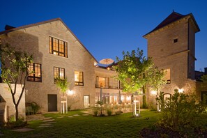 A stone building with multiple windows and a courtyard with outdoor seating. - Chez Gratien (Villeneuve)