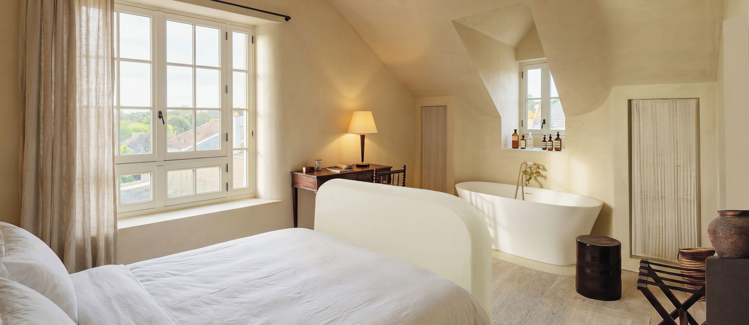 Une chambre d’hôtel avec un lit, un bureau, une lampe, une baignoire et une fenêtre.