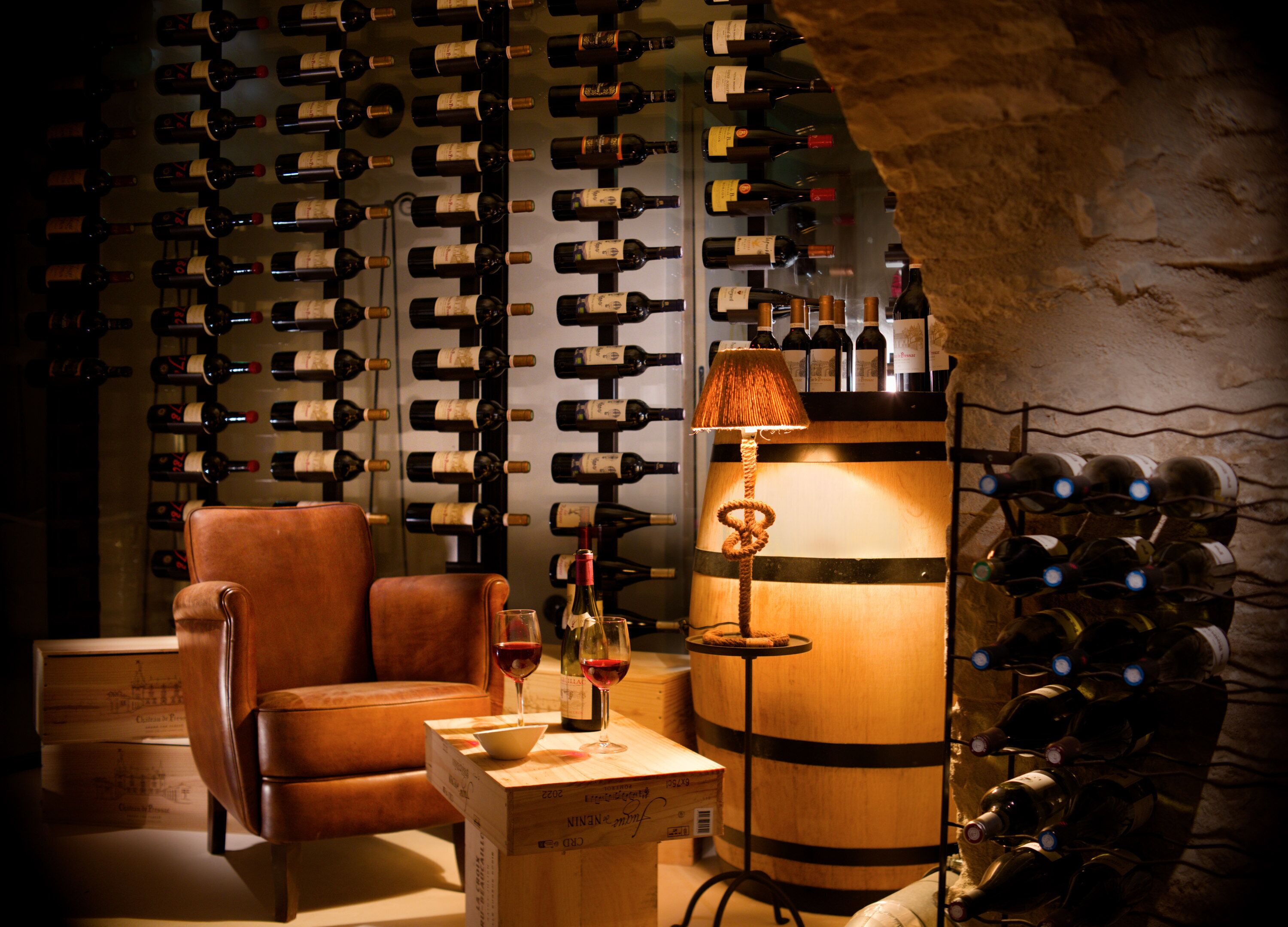 A wine cellar with a wooden barrel, a leather chair, and a table with wine bottles and glasses.