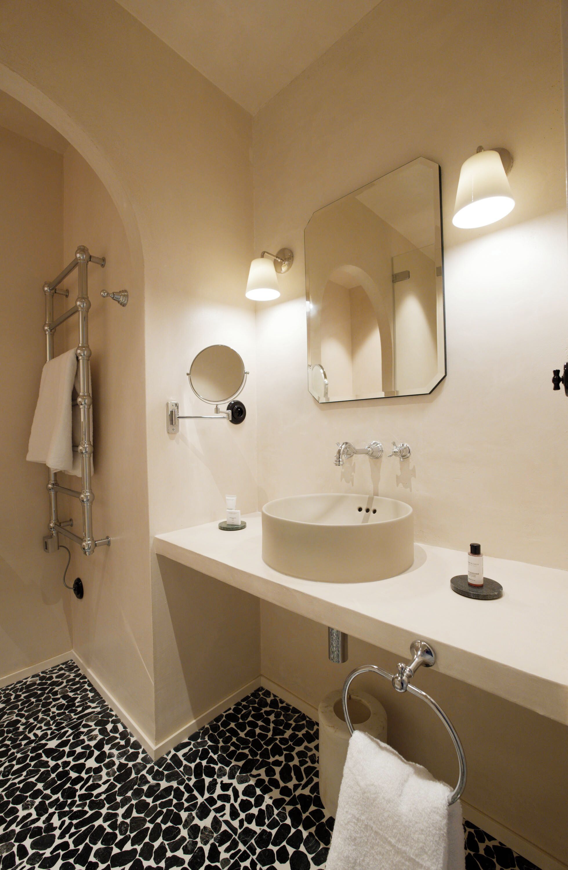 Un baño con un lavamanos blanco, un espejo redondo, un perchero y un piso con diseño blanco y negro.