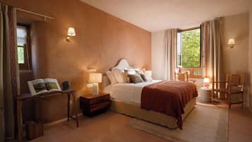Un dormitorio con una cama grande, lámparas de noche, una mesita de noche, una silla y una ventana con cortinas.