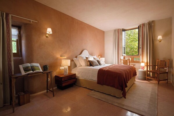 Un dormitorio con una cama grande, lámparas de noche, una mesita de noche, una silla y una ventana con cortinas.