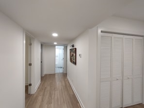 Ein Flur mit Holzboden, weißen Wänden, einer Tür mit Fensterglas und einem weißen Schrank mit Lüftungsklappen.