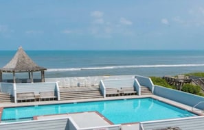 Ein Poolbereich mit Meerblick, eine Laube und eine Terrasse mit Stühlen.
