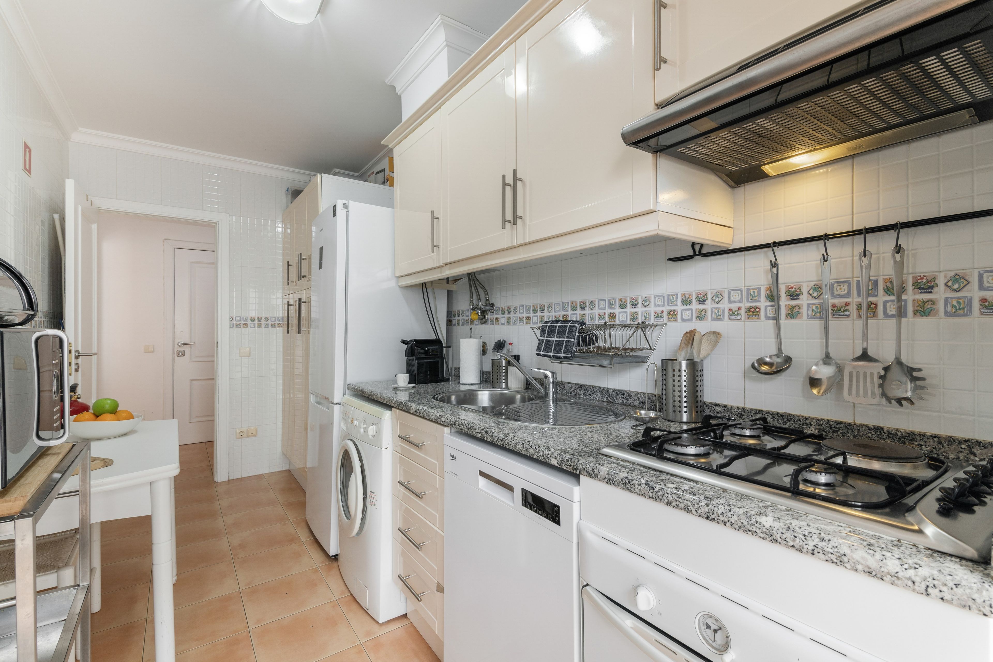 Cocina compacta con armarios blancos, horno empotrado, estufa a gas y lavadora.