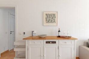 Eine Küche mit Holzausziehtisch, einem weißen Schrank, einem gerahmten Kunstwerk, einer Weinflasche und zwei Gläsern.