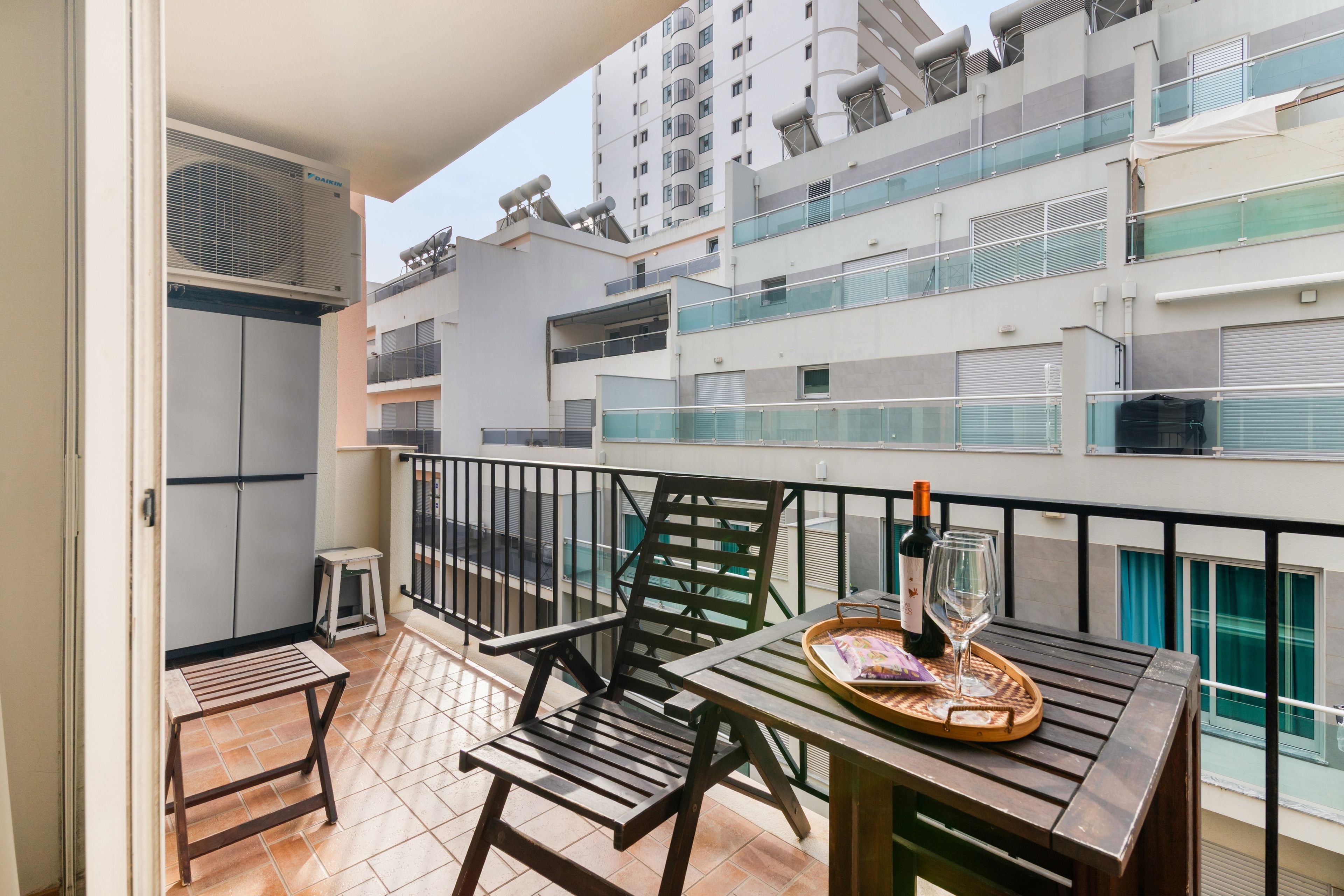 A balcony with a wooden table, chairs, a bottle of wine, and a tray.