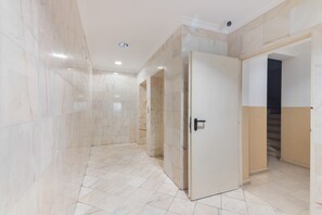 En hall med väggar klädda i marmor och ett klinkergolv, som leder fram till en dörr med ett handtag.
