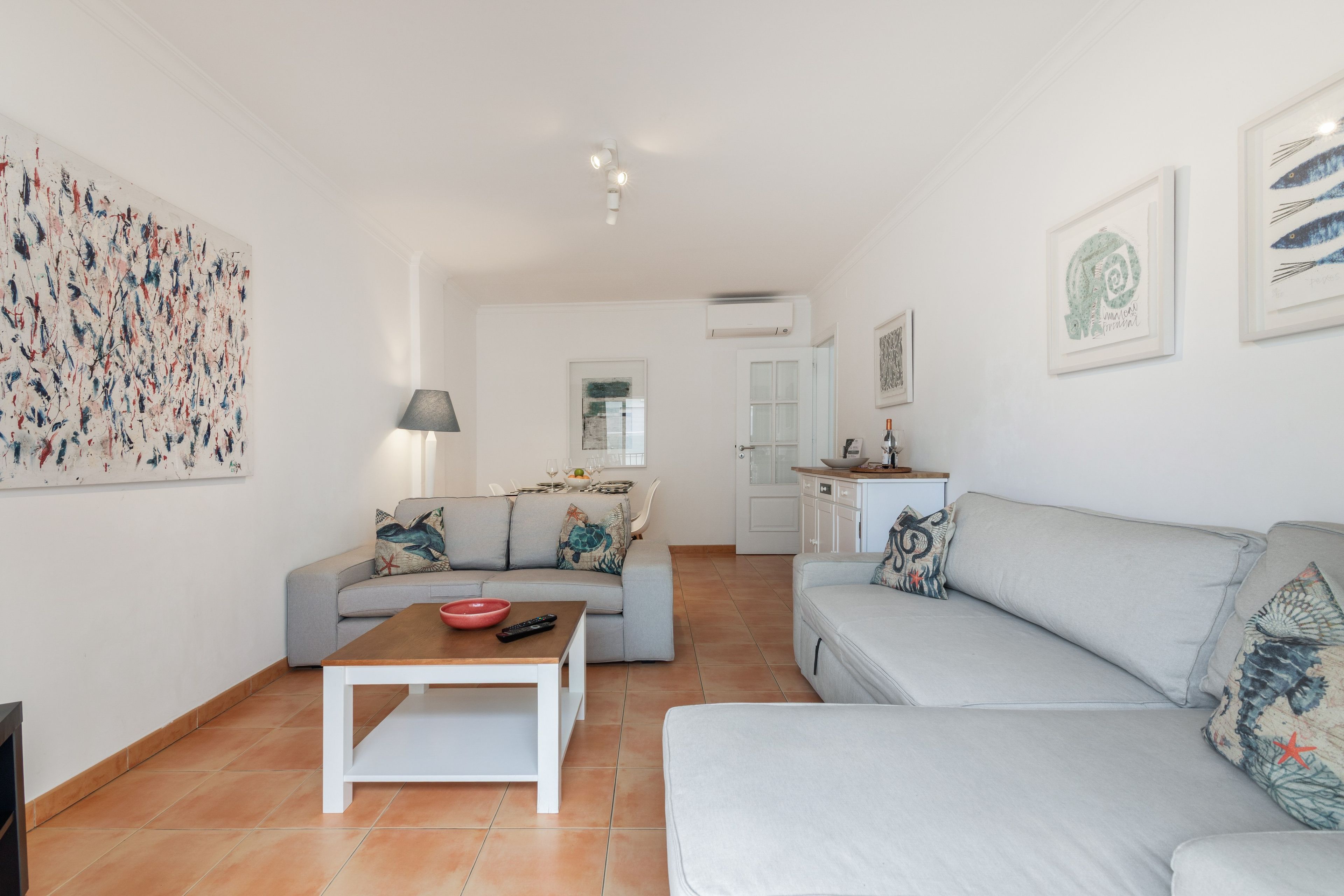 En moderne stue med en grå sofa, et sofabord og et spiseområde med et bord dækket til to personer.