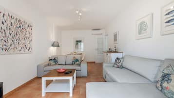 En moderne stue med en grå sofa, et sofabord og et spiseområde med et bord dækket til to personer.