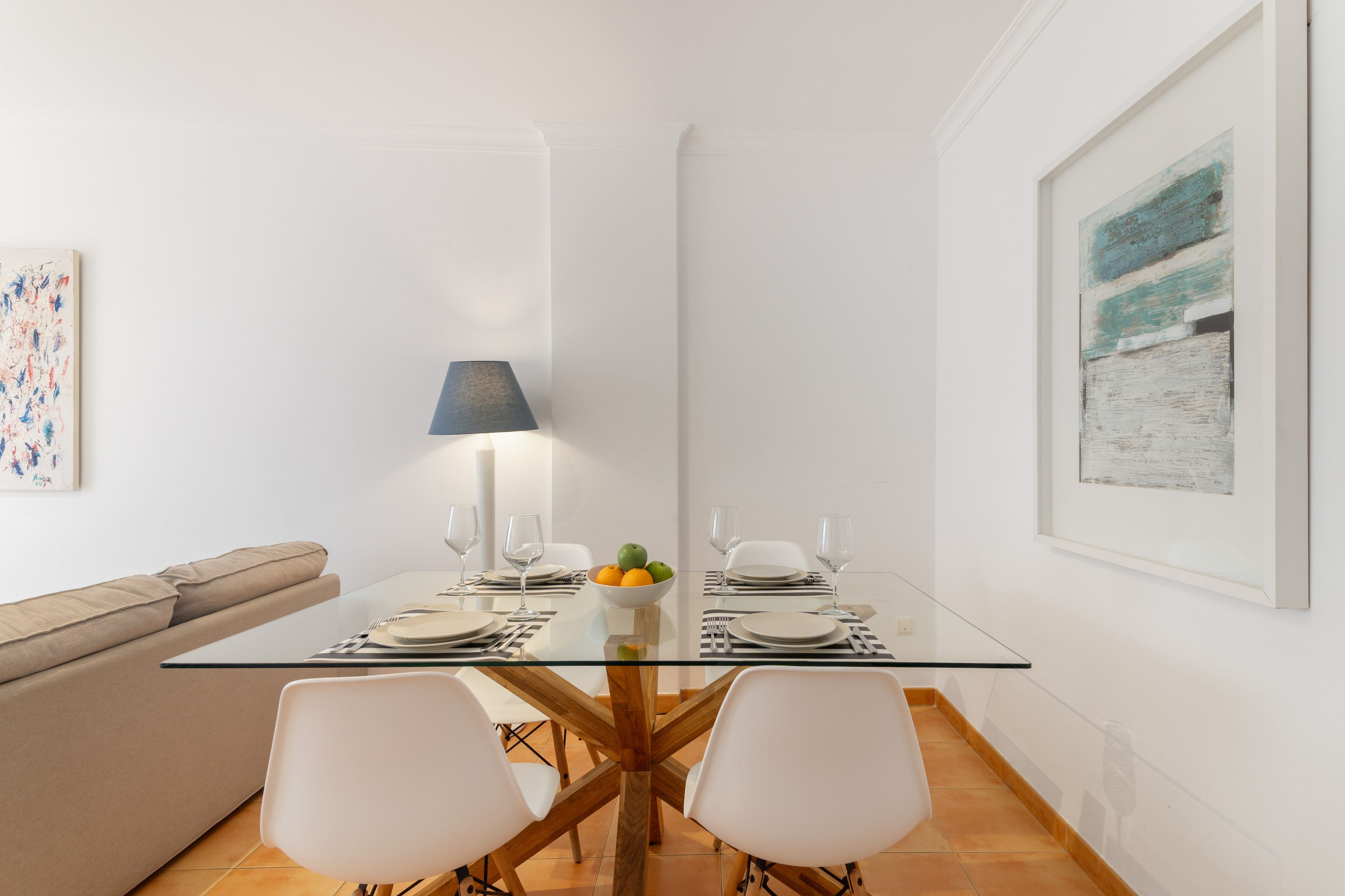 Een moderne eethoek met een glazen tafel, witte stoelen en een schaal fruit.