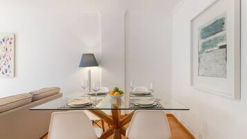Een moderne eethoek met een glazen tafel, witte stoelen en een schaal fruit.