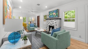 Ein Wohnzimmer mit Kamin, grünen Sofas, einer blauen Globenlampe und Bildern an den Wänden.