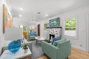 Ein Wohnzimmer mit Kamin, grünen Sofas, einer blauen Globenlampe und Bildern an den Wänden.