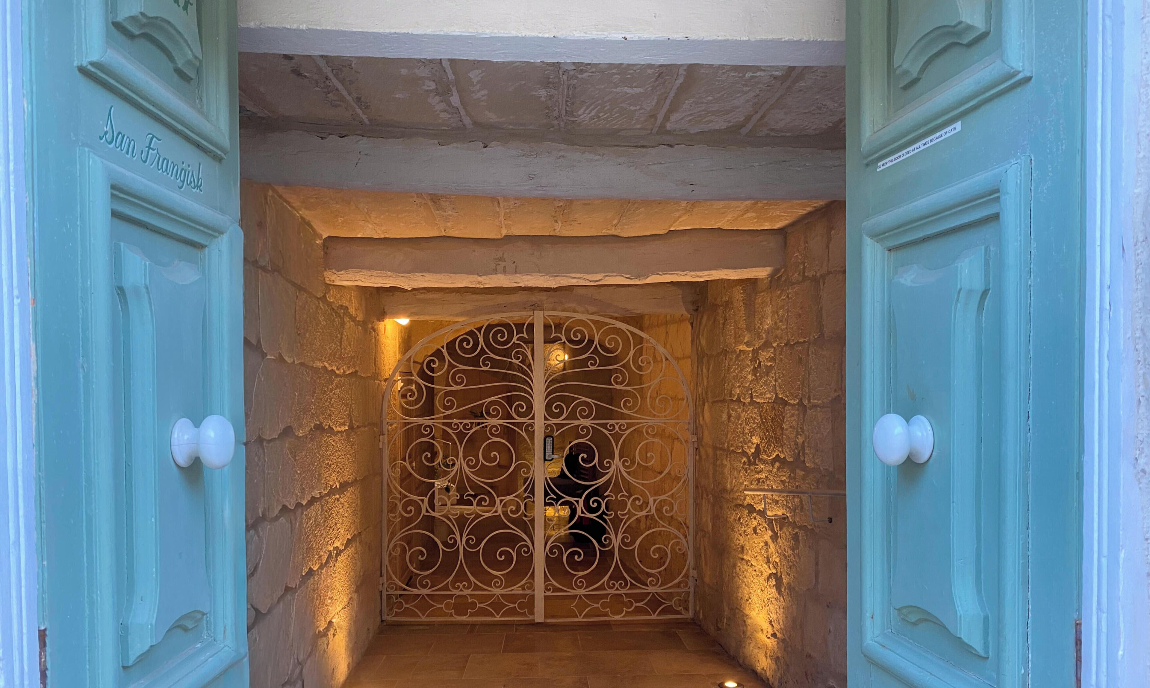 Une porte surmontée d’un portail en métal décoratif, un mur de pierre et une enseigne indiquant « San Francisco ».