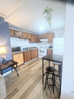A kitchen with wooden cabinets, a stove, microwave, and a hanging plant. - 1 bedroom pet friendly apartment on the first floor <br>- FREE parking<br>- ACs <br>- 7 minute walk from the beach.<br>- sleeps 3<br>- Queen bed and futon<br>- smart TV<br>- fast wifi<br>nroom before heading down to the beach! (Old Orchard Beach)