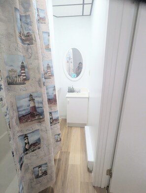 A narrow hallway with a white sink, a mirror, and a patterned shower curtain. - 1 bedroom pet friendly apartment on the first floor <br>- FREE parking<br>- ACs <br>- 7 minute walk from the beach.<br>- sleeps 3<br>- Queen bed and futon<br>- smart TV<br>- fast wifi<br>nroom before heading down to the beach! (Old Orchard Beach)