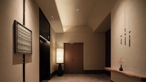A hallway with a wooden door, a wall-mounted sign, a floor lamp, and a small shelf with a vase. - Atour Hotel Nanjing Jianye (Nanjing)