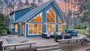 Une grande maison bleue avec une terrasse, de grandes fenêtres et du mobilier d’extérieur.