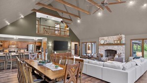 Un vaste espace de vie aménagé dans un style loft, comprenant une table à manger, des chaises en bois, un canapé blanc, une cheminée en pierre et un balcon.