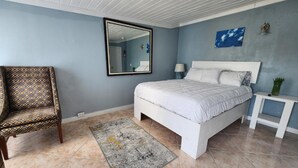 Ein Schlafzimmer mit einem Bett, einem Sessel, einem Nachttisch, einem Spiegel und einem Wandbild.