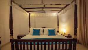 Una cama con dosel, una mesita de noche con lámpara y otro mueble auxiliar con un teléfono.