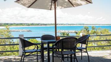 Um terraço com mesa e cadeiras, com vista para a praia e o mar.