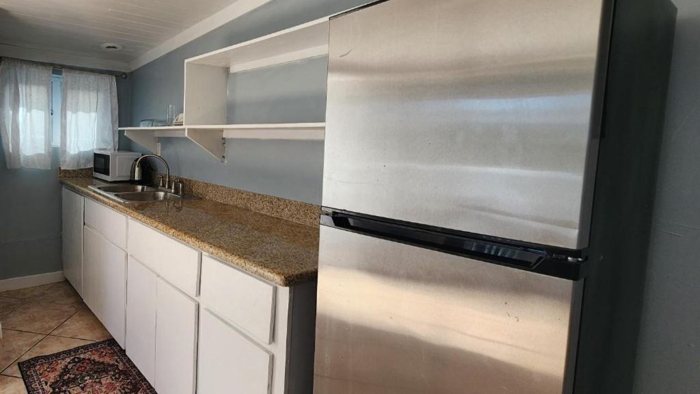 Una cocina con gabinetes blancos, un refrigerador de acero inoxidable, un microondas y un lavamanos.
