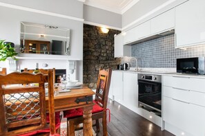 Una cocina moderna con muebles blancos, una pared de acento de piedra y un comedor con mesa y sillas de madera.