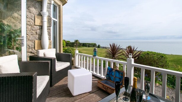 Ein Balkon mit Korbmöbeln, einem weißen Tisch und Blick aufs Meer.