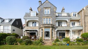 Ein großes, mehrstöckiges Haus mit einer Steinaußenfassade, mehreren Balkonen und einem gepflegten Garten.