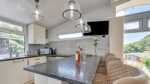 Ett modernt kök med en central köksö, inbyggda vitvaror och ett stort fönster med utsikt över omgivningen.