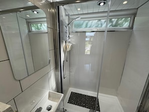 A modern bathroom with a glass-enclosed shower, a sink with a mirror, and a small window.