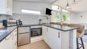 Ett modernt kök med inbyggd ugn, mikrovågsugn och kaffebryggare, en stor köksö med sittplatser och hängande lampor.